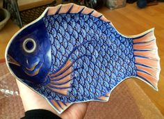 a hand holding a blue and orange fish shaped plate