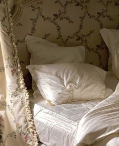 an unmade bed with white linens and flowers on the headboard is shown