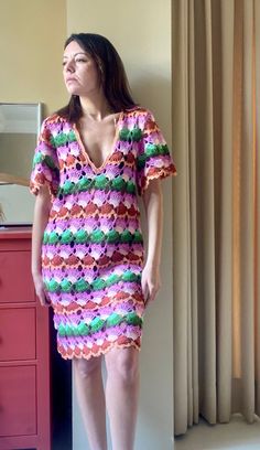 a woman standing in front of a mirror wearing a colorful crochet dress and sandals