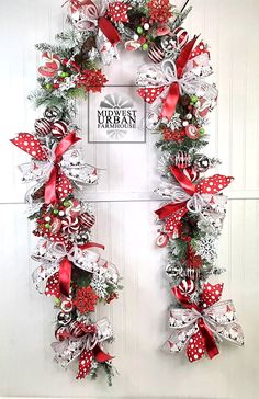 a christmas wreath hanging on the front door with red and white ribbons, ornaments and bows