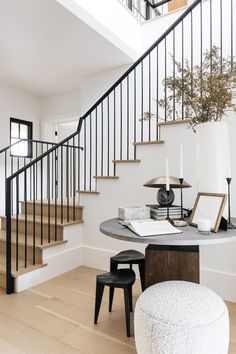 a table with two stools and a vase on it in front of a stair case