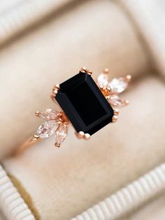 a black diamond ring sitting on top of a white velvet cushioned box with gold accents