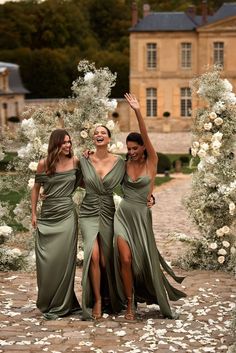 three women in long dresses standing next to each other at an outdoor ceremony with white flowers on the ground