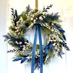 a wreath hanging on the front door with blue ribbon and white berries, greenery and bells