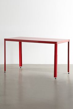 a red table sitting on top of a cement floor next to a white wall in an empty room