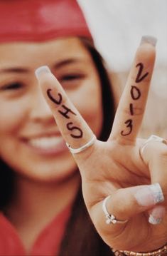 a woman in graduation cap and gown holding up two fingers with the word peace written on them