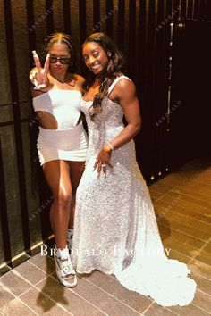 two women posing for the camera in white dresses and one is holding her hand up