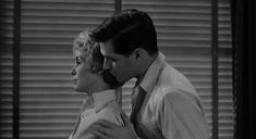 a man and woman standing next to each other in front of blinds