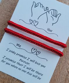 two red string bracelets sitting on top of a piece of paper next to a card