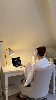 a woman sitting in a chair with headphones on and looking at a laptop computer