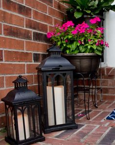 two black lanterns sitting on top of a brick floor next to a potted plant