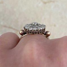 a close up of a person's hand holding an old fashioned diamond engagement ring