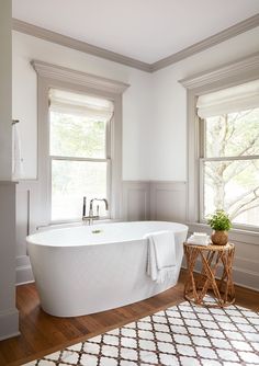 a large white bath tub sitting in a bathroom next to two windows and a rug on the floor