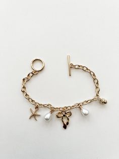 Gold charm bracelet. Charms include pearls, starfish, bow and acorn. Toggle Clasp. Gold Toggle Bracelet, How To Make A Charm Bracelet, Gold Pandora Bracelet, Charm Bracelet Charms, Pearl Charm Bracelet, Bracelet Packaging, Gold Girl, Pink Canvas, Bracelet Charms