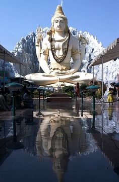 a large white statue sitting in the middle of a pool surrounded by buildings and mountains