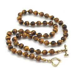 Tiger's Eye Necklace with Gold Plated Toggle Clasp Approx. 18 1/2" long Bead Size : 6mm Strung and knotted on silk cord Handcrafted at Beads of Paradise NYC Tiger’s Eye is a form of Chalcedony quartz, but is what is a known in mineralogy as a pseudomorph. The term comes from the Greek for "false form." Pseudomorphs form when one mineral replaces another. It began as the fibrous blue mineral called Crocidolite, which is made up of iron and sodium. The Crocidolite was gradually transformed into wh Gold Jewelry With Hand-knotted Round Beads, Round Beads Single Strand Lariat Necklace As Gift, Adjustable Single Strand Lariat Necklace With Round Beads, Lariat Necklace With Round Beads As Gift, Gold Hand-knotted Necklace For Gift, Gold Hand Knotted Necklace For Gift, Adjustable Lariat Necklace With Gemstone Beads, Beaded Necklaces With Round Beads And Toggle Clasp, Gift Beaded Necklaces With Toggle Clasp And Round Beads