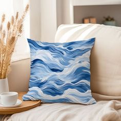 a blue and white pillow sitting on top of a couch next to a coffee cup