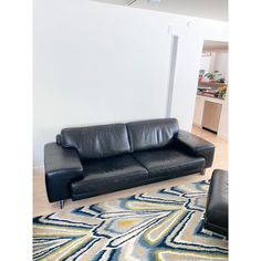 a black leather couch sitting on top of a rug in a living room next to a white wall