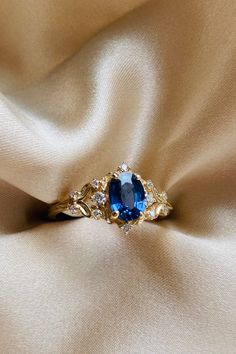 a blue and white diamond ring sitting on top of a beige satin fabric with gold accents