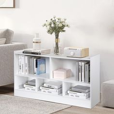 a white book shelf with books on it and a vase full of flowers in the corner