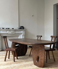 a wooden table with chairs around it in front of a fire place and white walls