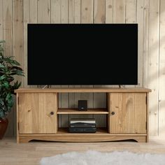 a flat screen tv sitting on top of a wooden entertainment center next to a potted plant