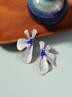 two blue and white flower shaped earrings on a wooden surface next to a vase with flowers in it