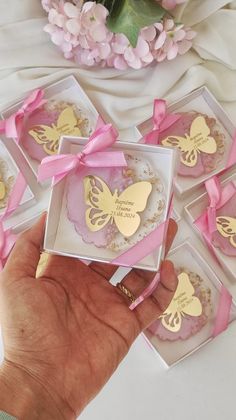 a hand holding a box with some gold butterflies on it and pink ribbon around the boxes