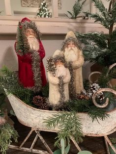 three santas in a sleigh with pine cones and evergreen branches on top