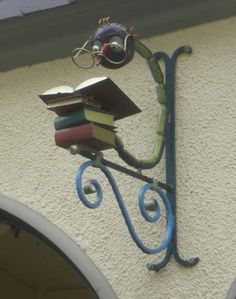 there is a sign with books attached to the side of this building that has a clock on it