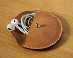 an apple earbud in a leather case on a wooden table with the cord plugged into it