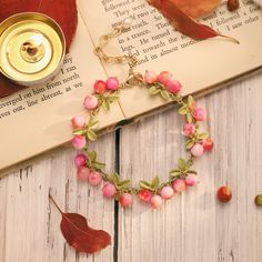 a bracelet with pink flowers and leaves on top of an open book next to a leaf