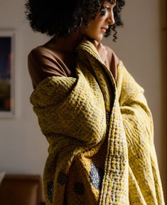 a woman wrapped in a yellow blanket looking off into the distance with her hands on her hips