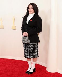 a woman standing in front of a red carpet wearing a black jacket and skirt with white socks