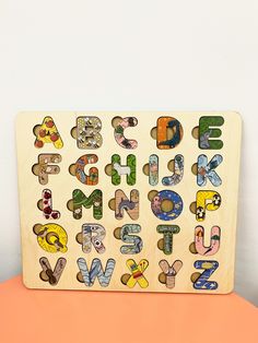 a wooden alphabet puzzle sitting on top of an orange table next to a white wall