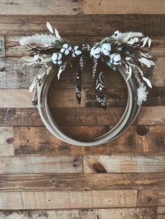 a wreath with white flowers and feathers hanging on a wooden wall