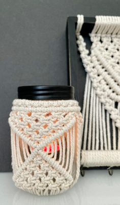 a white crocheted candle holder with a black lid next to a gray wall