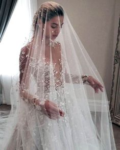 a woman in a wedding dress with a veil on her head and hands behind her back