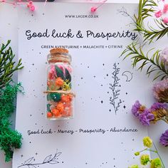 an assortment of flowers and rocks in a glass jar on top of a paper with the words good luck & prosperity