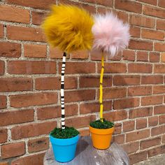 two potted plants with yellow and pink feathers on them sitting next to a brick wall