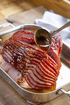 the ham is being drizzled with sauce on it's side while sitting in a metal pan