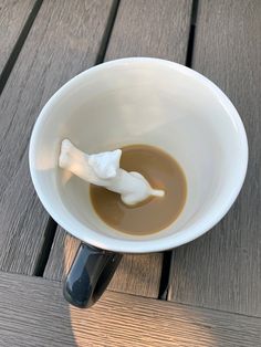 a white cup filled with liquid sitting on top of a wooden table next to a spoon