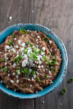 a blue bowl filled with refried beans on top of a wooden table and topped with shredded parmesan cheese