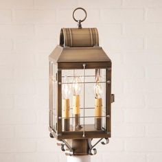 an old fashioned lantern with three lit candles on the front and side of it, against a white brick wall