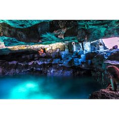 a person sitting on the edge of a cave next to a body of blue water