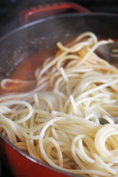 some noodles are being cooked in a pan on the stove top with tongs and water