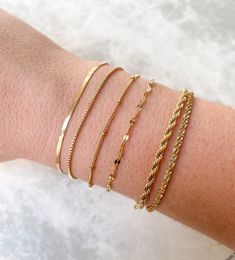 Dainty stainless steel bracelets that can be layered / stacked are ideal for mixing and matching! Combine your favorite gold link chains to create a seamless look. Plus, they are tarnish resistant and waterproof; you can wear them to the pool or gym and they won't tarnish! Herringbone (2.5 mm): 7" +1.5" extender (Clasp & Jump Ring Excluded) Box: 6.75” + 2" extender Satellite: 6" + 1.5" extender Rope (2.5 mm): 6.25" + 2" extender Dainty Gold Bracelet, Bracelet Box, Gold Link Chain, Gold Link, Gold Bracelets, Jewelry Lookbook, Minimalist Bracelet, Crown Jewels, Braided Bracelets