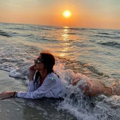 a woman laying on top of a sandy beach next to the ocean under a sunset