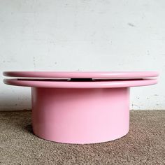 a pink round table sitting on top of a carpeted floor