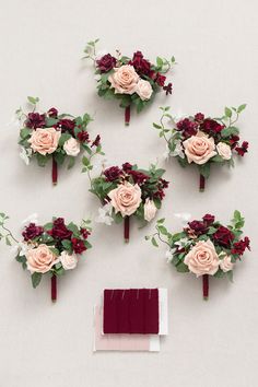 wedding bouquets and boutonnieres laid out on a white surface with burgundy napkin